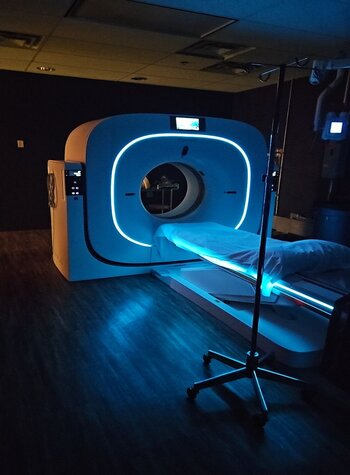 A picture of the CT machine with the lights off in the room, the CT machine has blue lighting on the front and underneath
